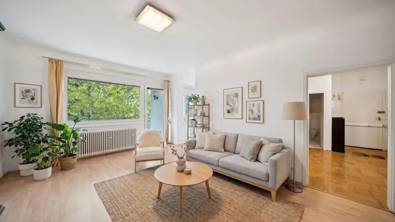 Helles Wohnzimmer mit Parkettboden, bequemer Couch und Zugang zum Balkon.