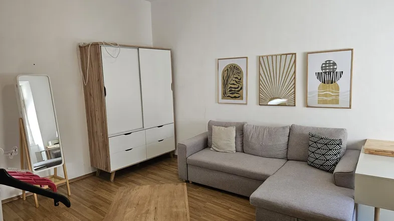 Helles Wohnzimmer mit beigem Sofa, Holzschrank und modernen Wandbildern, ideal zum Entspannen.