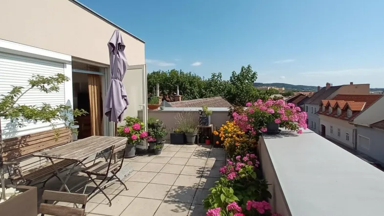 Geräumige Sonnenterrasse mit Holztisch, Stühlen und bunten Blumen, ideal zum Entspannen im Freien.