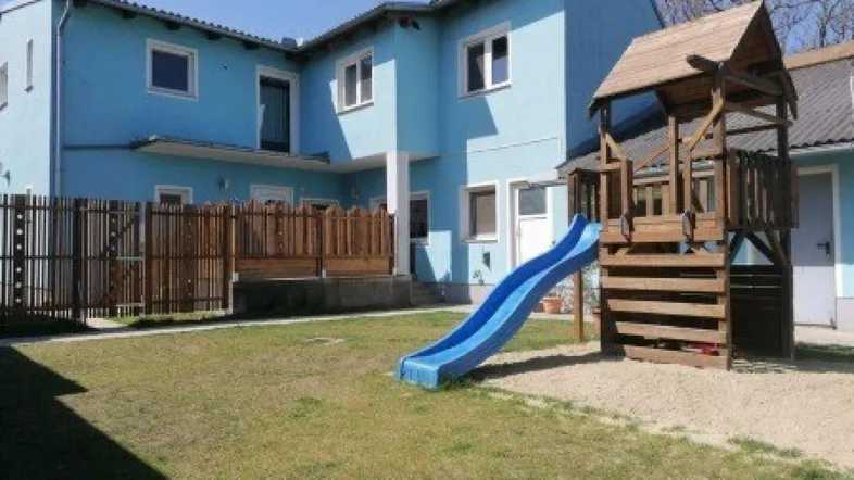 Blaues Gebäude mit großem Garten und Kinderspielplatz, ideal für Familien.