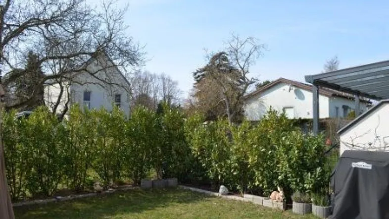 Gepflegter Gartenbereich mit Rasenfläche und Hecke, umgeben von weiteren Wohnhäusern unter blauem Himmel.