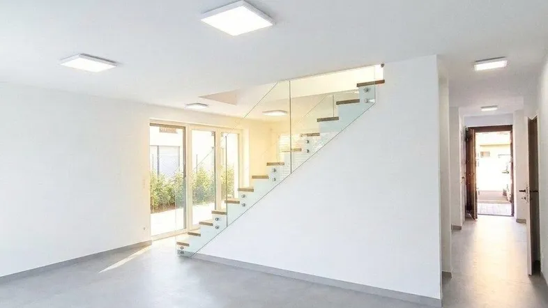 Heller, moderner Wohnbereich mit Betonboden, offener Treppe und Zugang zur Terrasse.
