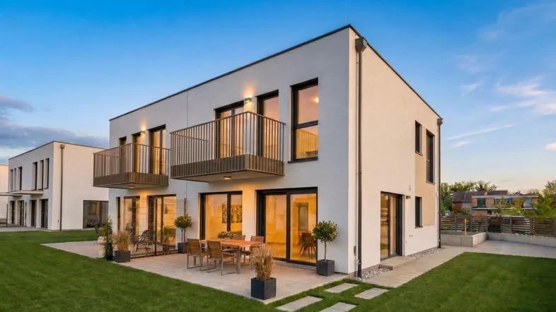 Modernes Einfamilienhaus mit weißer Fassade, Terrasse und Balkonen, umgeben von einem gepflegten Rasen.