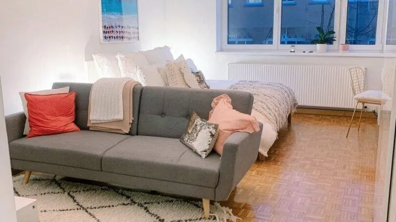 Helles Wohnzimmer mit modernem Sofa, Teppich und Parkettboden, gut beleuchtet durch große Fenster.