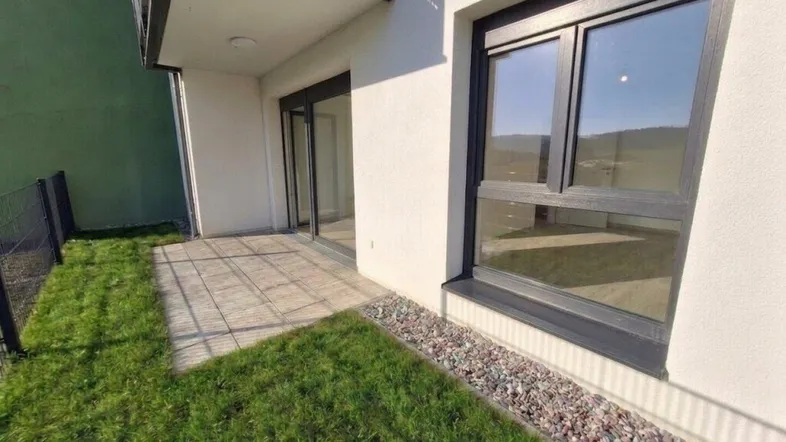 Ebenerdige Terrasse mit Rasenfläche und Zugang zu einem modernen Wohnbereich im Neubau.