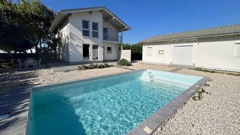 Weißes Haus mit modernem Pool und Kiesgarten unter blauem Himmel, ideal für Sommertage.