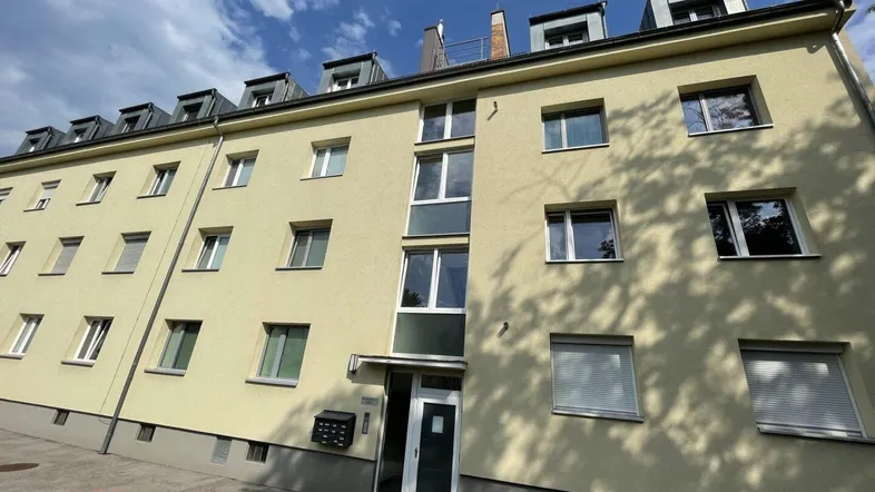 Mehrfamilienhaus mit gelber Fassade, vielen Fenstern und Dachgauben unter blauem Himmel.