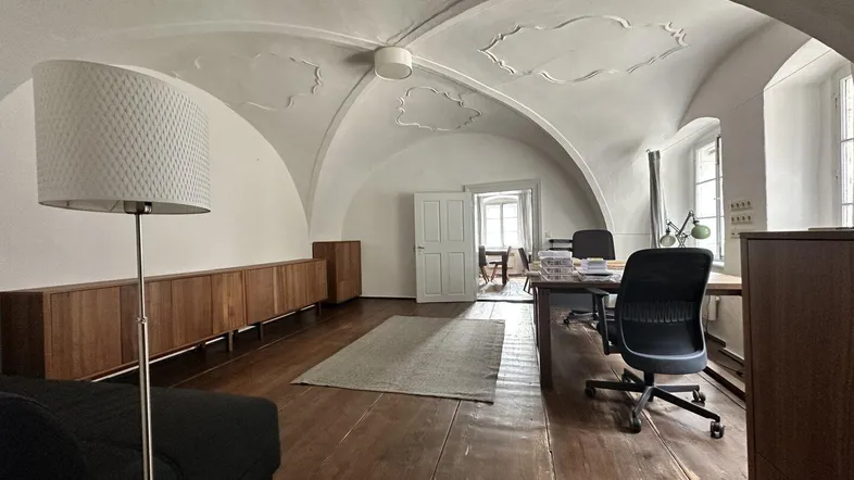 Geräumiges Büro mit beeindruckendem Gewölbedecke, Holzboden und natürlichem Lichteinfall durch große Fenster.