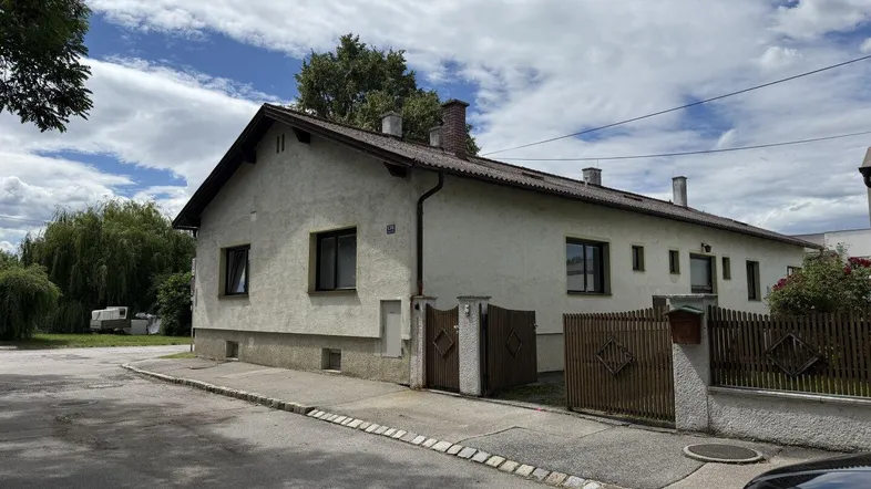 Einfamilienhaus mit heller Fassade und Satteldach, umgeben von Grünflächen und einer Straße.
