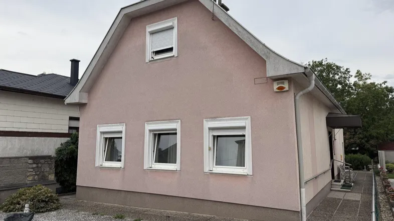 Einfamilienhaus mit rosafarbener Fassade, weißen Fenstern und Satteldach.