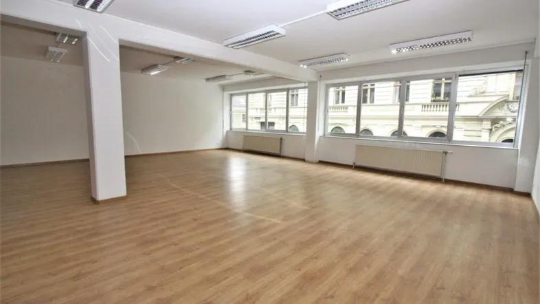 Geräumiges, leeres Büro mit großen Fenstern, die viel Tageslicht hereinlassen und einen Blick auf die Straße bieten.