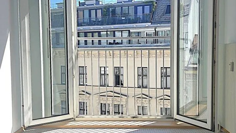 Heller Raum mit großen Fenstern, die sich zu einem französischen Balkon mit Stadtblick öffnen.