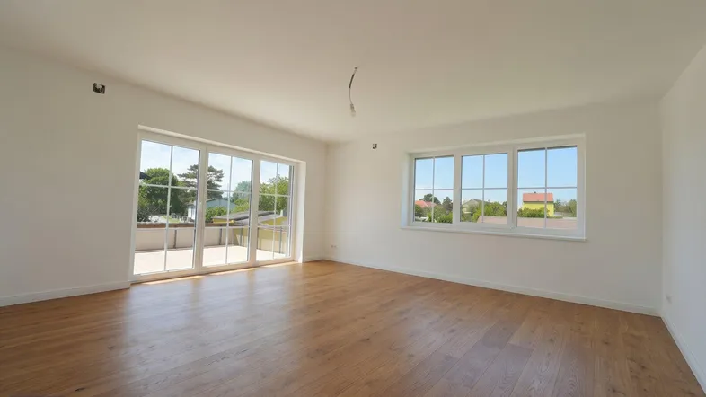 Helles Wohnzimmer mit Holzboden und großen Fenstern, die viel Tageslicht hereinlassen und Zugang zu einer Terrasse bieten.