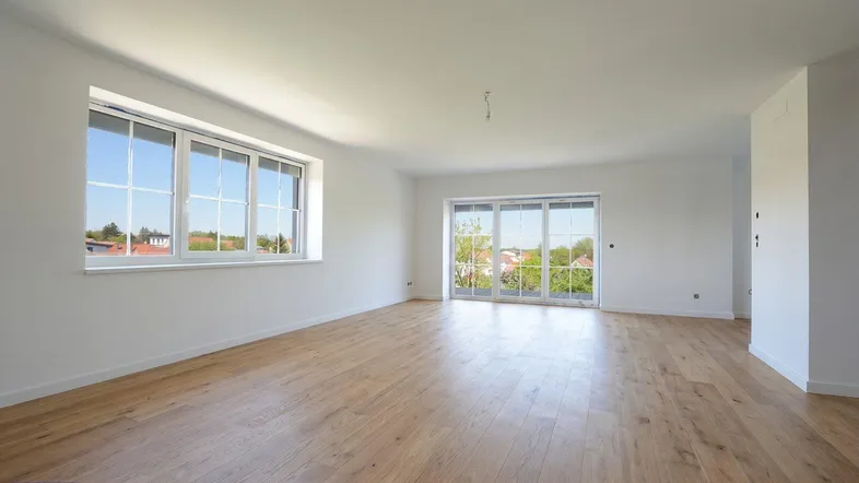 Geräumiges Wohnzimmer mit hellem Holzboden, großen Fenstern und Zugang zu einem Außenbereich.