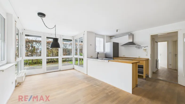 Helles, offenes Wohnzimmer mit Holzboden und großen Fenstern, die viel Tageslicht hereinlassen.