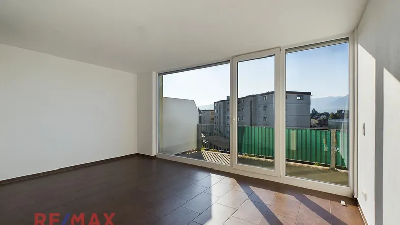 Helles Wohnzimmer mit großen Fenstern, Fliesenboden und Zugang zum Balkon.