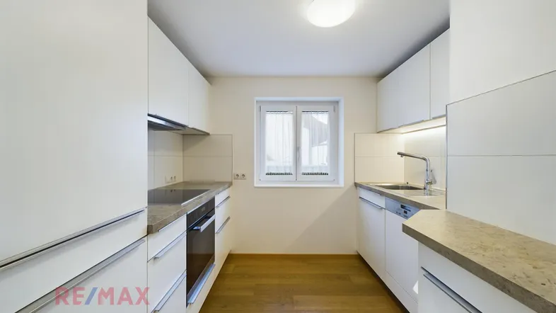 Moderne Küche mit weißen Schränken, Stein-Arbeitsplatte und hellem Holzfußboden.