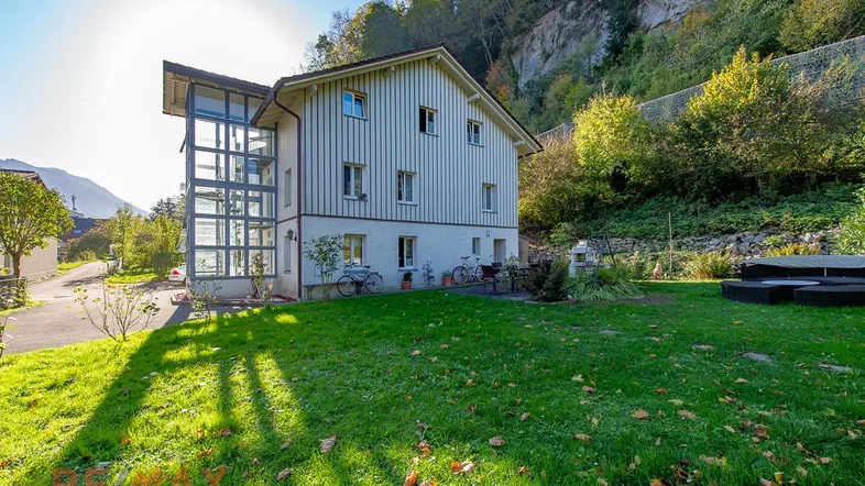Großzügiger Gartenbereich mit Rasenfläche und Sitzgelegenheit vor dem Haus mit Glasanbau.