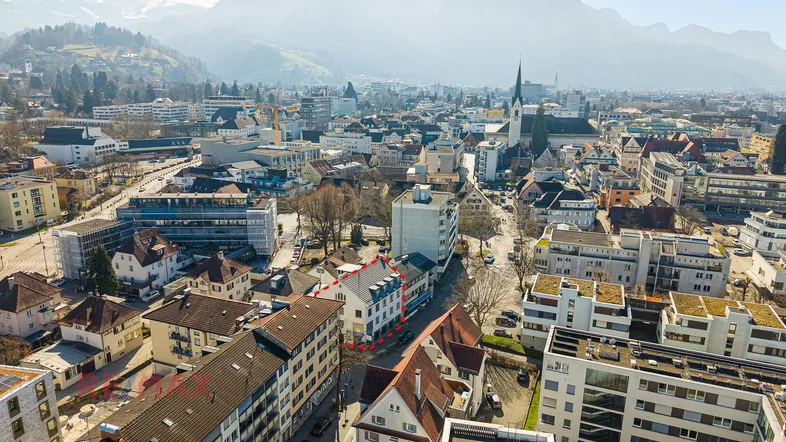 Luftaufnahme der Stadt mit dem umrandeten Gebäude und umliegenden Bergen im Hintergrund.