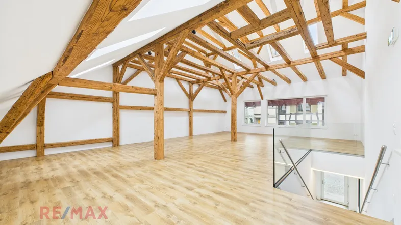 Geräumiger offener Wohnbereich im Dachgeschoss mit sichtbaren Holzbalken und hellem Laminatboden.