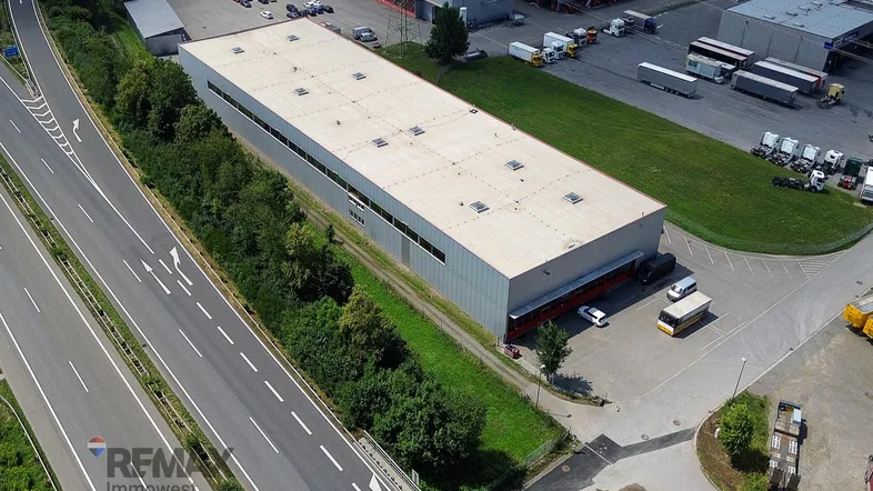 Luftaufnahme eines großen Industriegebäudes mit Flachdach, umgeben von einer Autobahn und weiteren Gewerbeflächen.