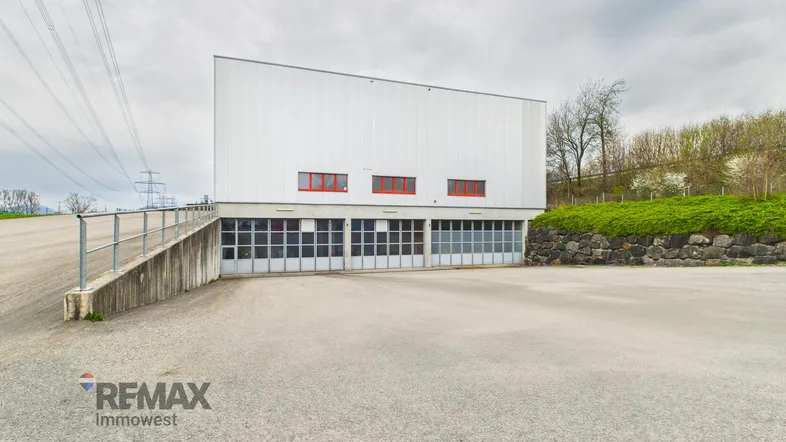 Modernes Industriegebäude mit mehreren Garagentoren und einer Zufahrtsrampe unter bewölktem Himmel.