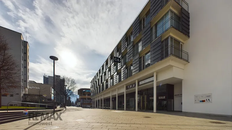 Moderne Geschäfts- und Wohngebäude mit großen Fenstern und Ladenfronten entlang einer städtischen Straße.