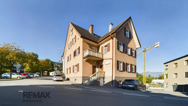 Traditionelles Gebäude mit mehreren Fenstern, einem kleinen Balkon und Blick auf die Berge.