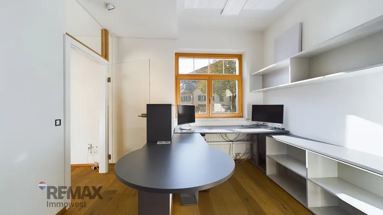 Modernes Büro mit Holzboden, Schreibtischen und Regalen, gut beleuchtet durch ein Fenster.