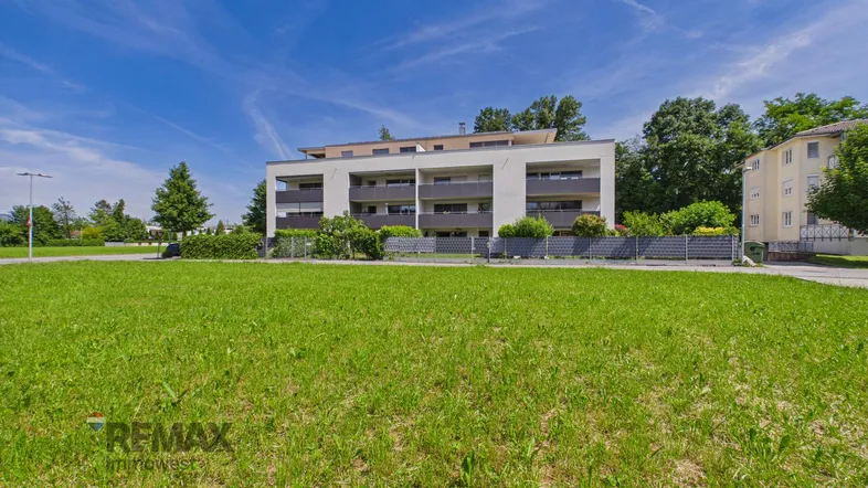 Modernes Mehrfamilienhaus mit Balkonen und gepflegter Grünfläche unter blauem Himmel.