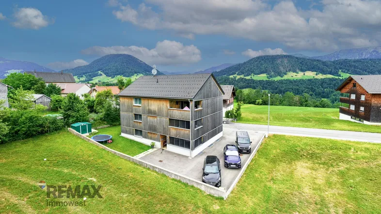 Luftaufnahme eines modernen Holzhauses mit Satteldach und Parkplätzen in ländlicher Umgebung.