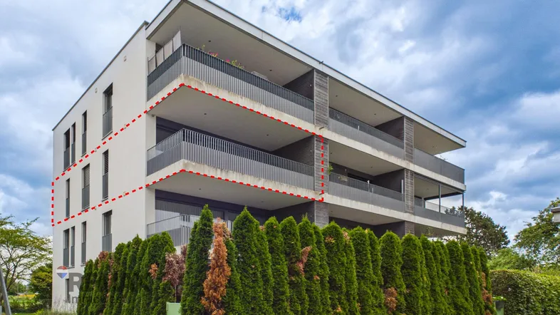 Moderne Wohnanlage mit mehreren Balkonen und gepflegter Hecke im Vordergrund unter bewölktem Himmel.