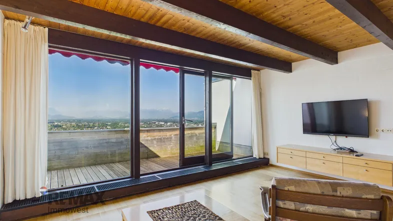 Helles Wohnzimmer mit Holzbalkendecke, Parkettboden und weitem Blick über die Stadt und Berge.