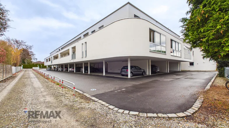 Modernes Mehrfamilienhaus mit offener Architektur und überdachten Parkplätzen im Erdgeschoss.