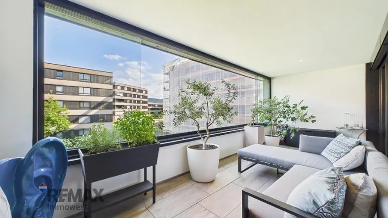 Heller, verglaster Balkon mit bequemen Loungemöbeln und Blick auf die Umgebung.