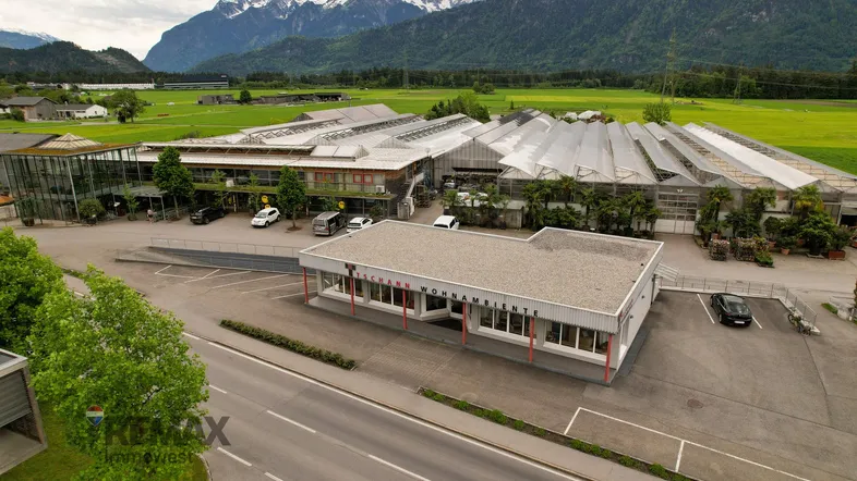 Luftaufnahme eines Gewerbekomplexes mit umliegenden Grünflächen und majestätischen Bergen im Hintergrund.