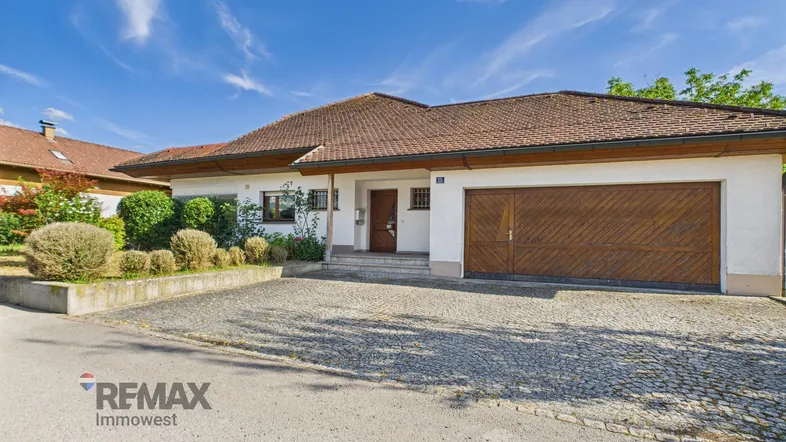 Einfamilienhaus mit gepflasterter Auffahrt und integrierter Garage unter blauem Himmel.