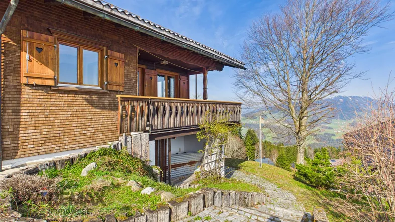 Traditionelles Holzhaus mit Balkon und malerischem Blick auf die umliegende Berglandschaft.