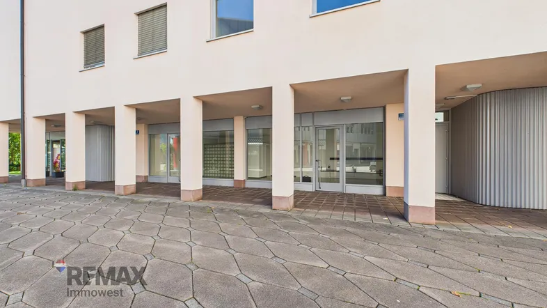 Die Außenansicht des Geschäftsgebäudes zeigt den Eingangsbereich mit Säulen und gepflastertem Vorplatz.