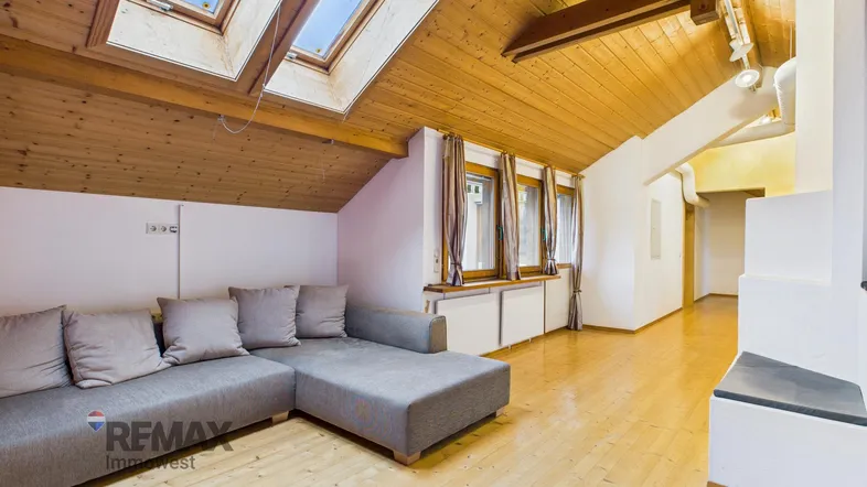 Helles Wohnzimmer mit gemütlichem Sofa, Holzboden und Dachschrägenfenstern, die viel Tageslicht hereinlassen.