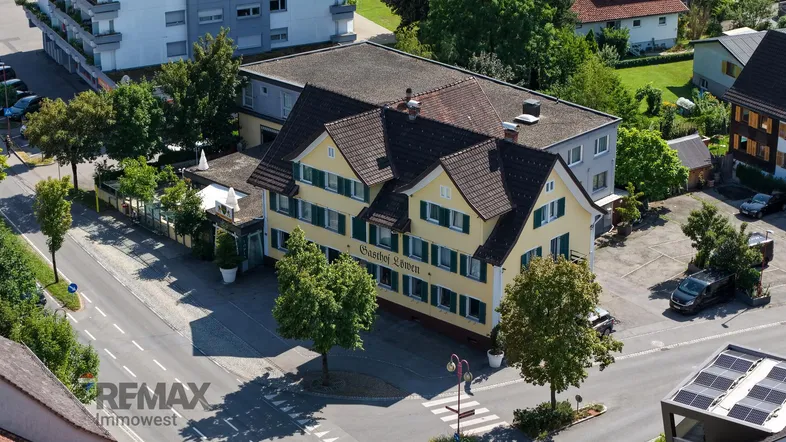 Luftaufnahme eines traditionellen Gasthofs mit gelber Fassade, umgeben von Bäumen und Straßen.