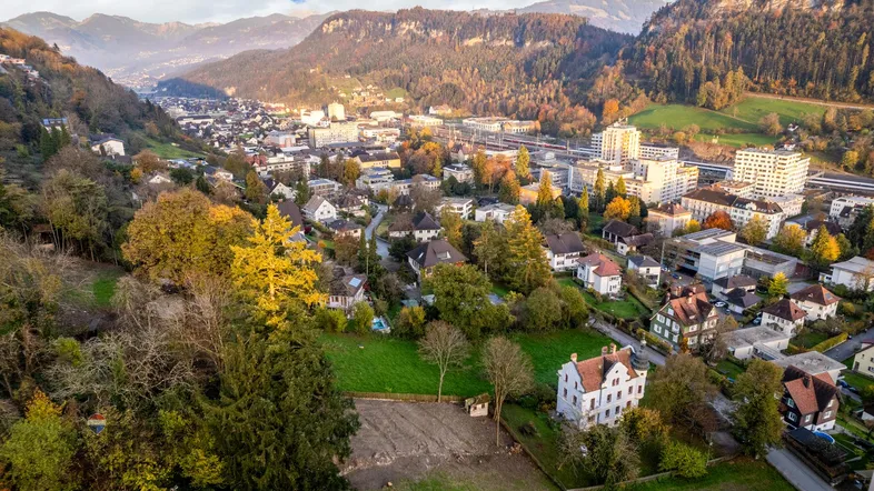 Panoramablick auf eine Stadt im Tal, umgeben von Bergen und herbstlicher Vegetation.