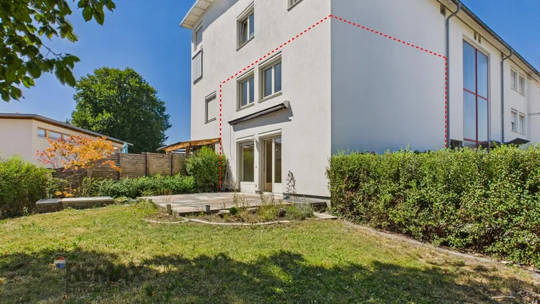 Weißes Mehrfamilienhaus mit Gartenbereich und Terrasse unter blauem Himmel.