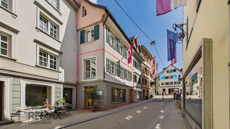 Historisches Gebäude an einer belebten Straße mit Geschäften und Wohnungen, umrandet von einer roten Linie.