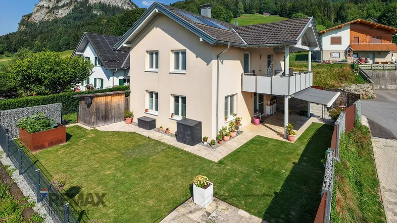 Freistehendes Einfamilienhaus mit gepflegtem Garten, Rasenfläche und Bergblick in ländlicher Umgebung.