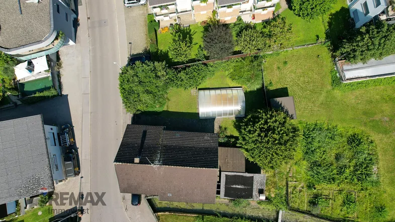 Luftaufnahme eines Einfamilienhauses mit großem Garten und Gewächshaus in einer Wohngegend.