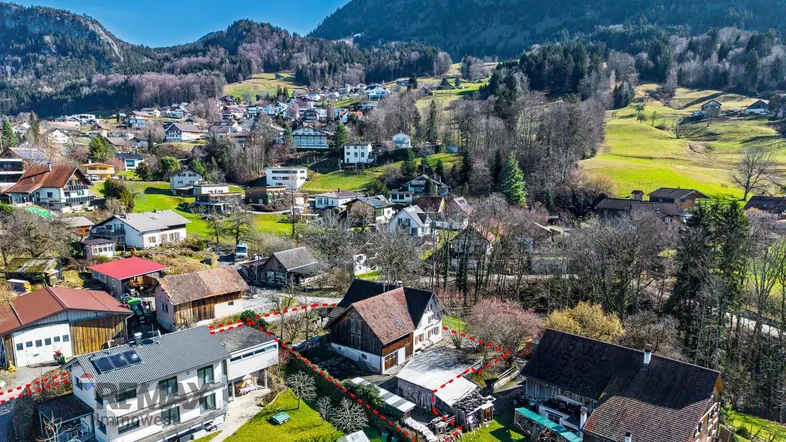 Luftaufnahme eines Hauses in ländlicher Umgebung mit Bergen im Hintergrund und angrenzenden Gebäuden.