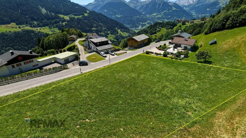 Luftaufnahme eines Grundstücks in den Bergen, umgeben von grünen Wiesen und Häusern.