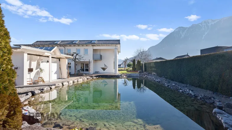 Großzügiger Gartenbereich mit einem natürlichen Schwimmteich und Blick auf die umliegenden Berge.