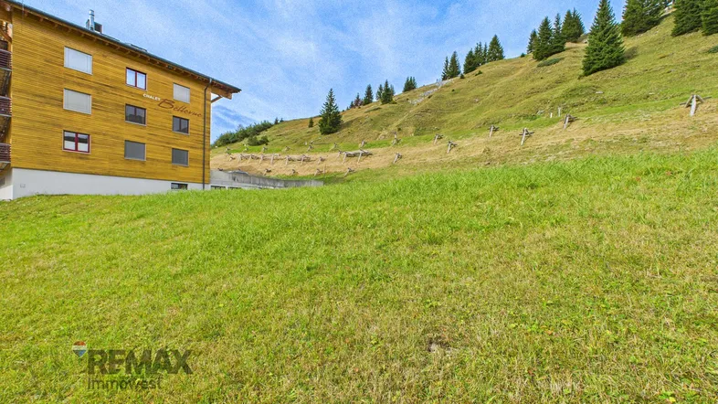 Gebäude mit Holzfassade und grüner Wiese im Vordergrund unter blauem Himmel.